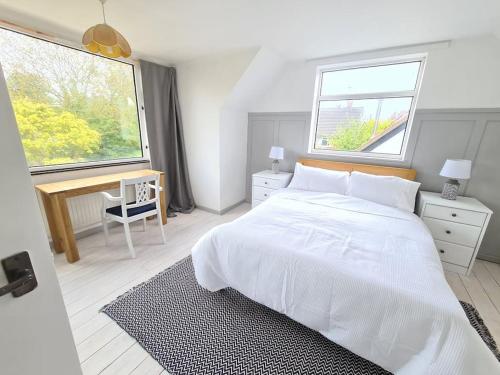 a white bedroom with a bed and a desk and two windows at Beach Chalet, Little Walsingham Norfolk in Little Walsingham
