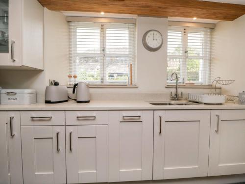 a kitchen with white cabinets and a clock on the wall at Jessamine Cottage in Ambleside