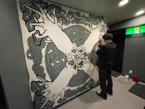 a man taking a picture of a painting on a wall at TenTen Guesthouse in Asakusa in Tokyo