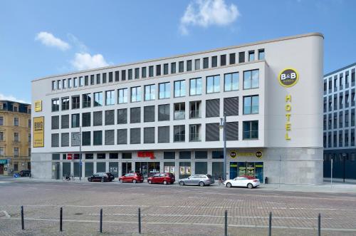 un grand bâtiment blanc avec des voitures garées devant lui dans l'établissement B&B Hotel Halle (Saale), à Halle-sur-Saale