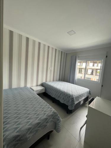 a hotel room with two beds and a window at Apto com Piscina, Estacionamento e Churrasqueira em Bombas - 2 dorms 6 pessoas - 300 metros do Mar in Bombinhas