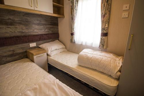 2 Betten in einem kleinen Zimmer mit Fenster in der Unterkunft Modern Caravan At Caldecott Hall With Decking In Norfolk, Sleeps 8 Ref 91068c in Great Yarmouth