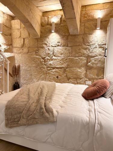 a bedroom with a white bed with a stone wall at MCC Argotti House in Il-Furjana