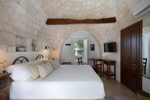 ロコロトンドにあるAgriturismo Masseria Aprileの白いベッドと石の壁が備わるベッドルーム1室