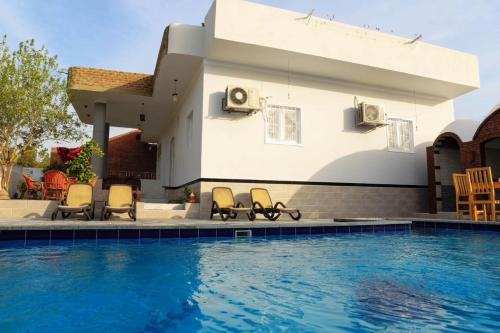 a house with a swimming pool and chairs next to a house at Happiness Guest House in Luxor