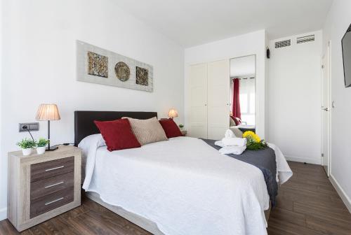 a white bedroom with a large bed with red pillows at Playa Victoria Paseo Marítimo 3 Rooms in Cádiz