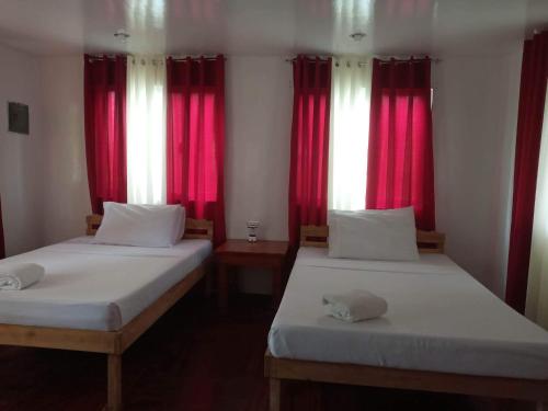 two beds in a room with red curtains at Bayay ni Nanay Bed & Breakfast in Magpupungko Beach Road in Pilar