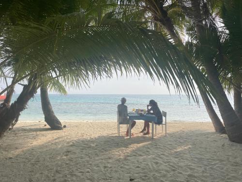 two people sitting at a table on the beach at Mandhoo Inn in Mandhoo