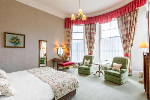 a bedroom with a bed and two chairs and a table at Cally Palace Hotel & Golf Course in Gatehouse of Fleet