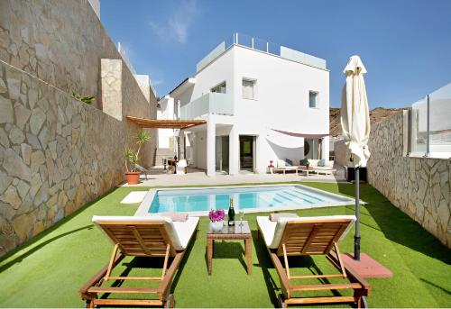 a villa with a swimming pool and two chairs and an umbrella at Escape to paradise luxury Poolvilla with ocieanview near Amadores in Mogán