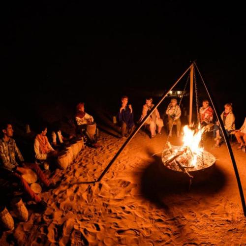 a group of people sitting around a fire in the sand at Merzouga heart camp in Merzouga