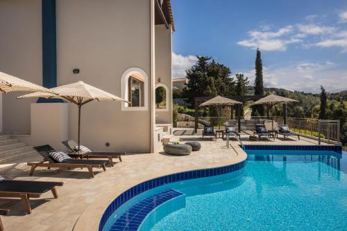 a pool with chairs and umbrellas next to a house at Luxury Villa Karmaniolos Fiskardo Kefalonia in Fiskardho