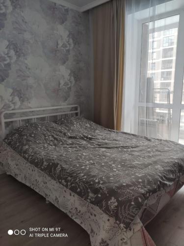 a bed sitting in a bedroom with a window at Квартира в ЖК Будапешт 10 мин от Аэропорта и ЭКСПО in Prigorodnyy