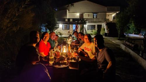 grupa ludzi siedzących w nocy przy stole w obiekcie Kurmanchal Village by THE GHAUR w mieście Almora