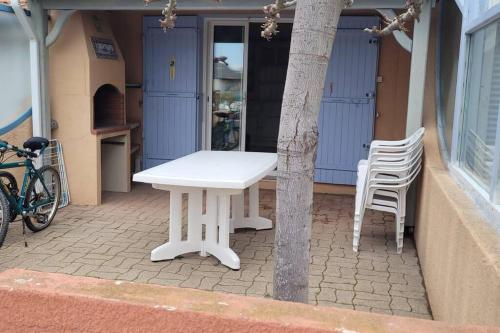 une table et des chaises blanches sur une terrasse avec un arbre dans l'établissement Charmante Maison de pêcheur, au Barcarès