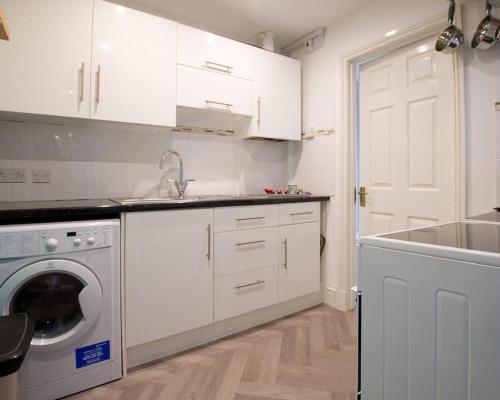 a kitchen with white cabinets and a washing machine at Cosy 1 Bedroom Apartment - Newbury High Street in Newbury