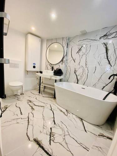 La salle de bains est pourvue d'une baignoire blanche et d'un mur en marbre. dans l'établissement L’intemporel, à Rouen