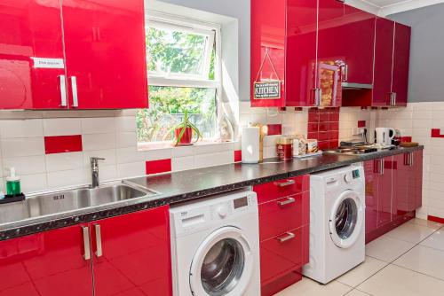 a red kitchen with a sink and washing machines at Shirley House 1, Guest House, Self Catering, Self Check in with smart locks, use of Fully Equipped Kitchen, Walking Distance to Southampton Central, Excellent Transport Links, Ideal for Longer Stays in Southampton