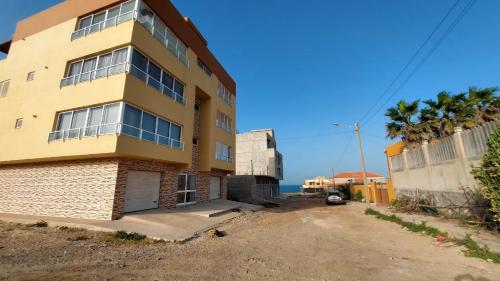 a yellow building with the ocean in the background at Apartamento F3, Lazareto - Mindelo in Mindelo