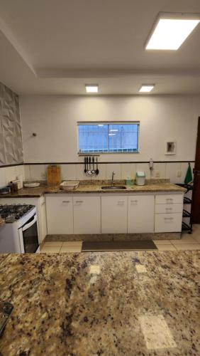 a large kitchen with white cabinets and a window at Casa confortável pertinho da praia com garagem e quintal in Rio das Ostras