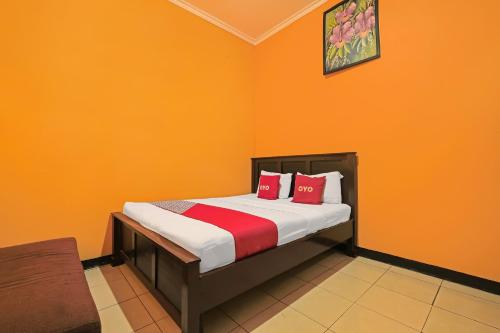 a bedroom with orange walls and a bed with red pillows at OYO 92486 Hotel Permata 3 in Salatiga