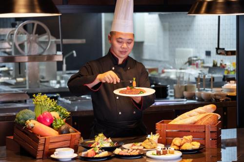 a chef in a kitchen holding a plate of food at Four Points by Sheraton Chongqing, Yongchuan in Yongchuan