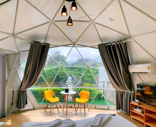 a room with a large window with yellow chairs and a table at Glamping hill khaoyai in Khao Yai