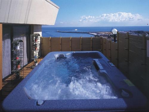 bañera de hidromasaje en un balcón con vistas al océano en el fondo en Atami Tamanoyu Hotel, en Atami