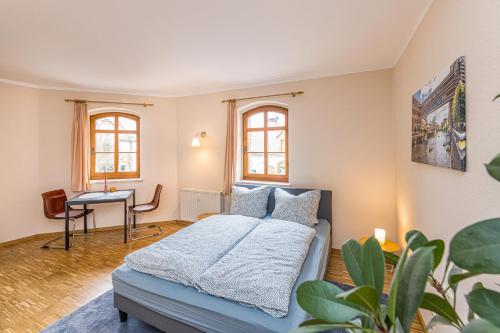 a bedroom with a bed and a table and windows at Stadtgut Mölkau Rooms & Apartments in Leipzig