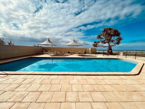 a swimming pool with tables and umbrellas at Absolute Beachfront Luxury - Heated Pool - 75 TV in Gold Coast