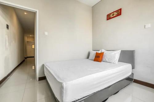 a white bedroom with a bed with an orange pillow at KoolKost at Bypass Nusa Dua in Nusa Dua