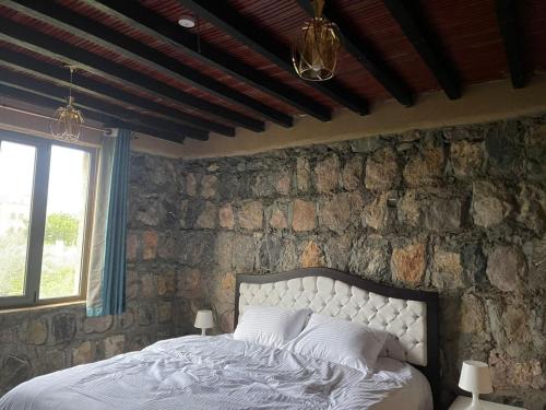 1 dormitorio con 1 cama con pared de piedra en Rose Guesthouse en Al ‘Aqar