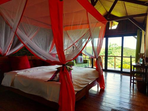 1 dormitorio con 1 cama con cortinas rojas y blancas en Nature Lodge en Diego Suarez