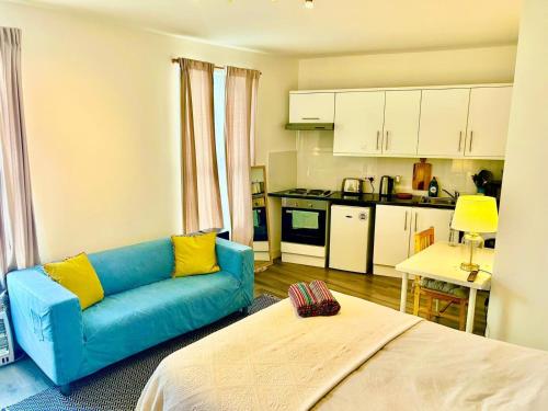 a living room with a blue couch and a kitchen at Studio 5 mins walk from Seven Sisters Station in London