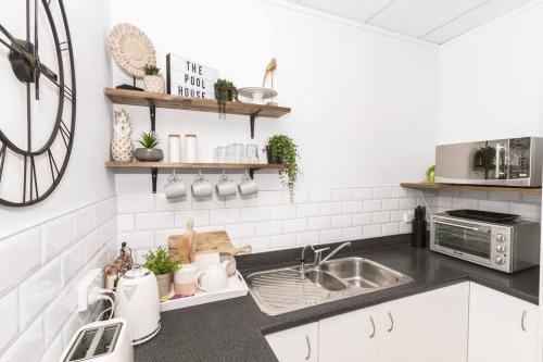 a kitchen with white cabinets and a sink and a clock at Rustling Oaks NZ Boho Pool House in Cambridge