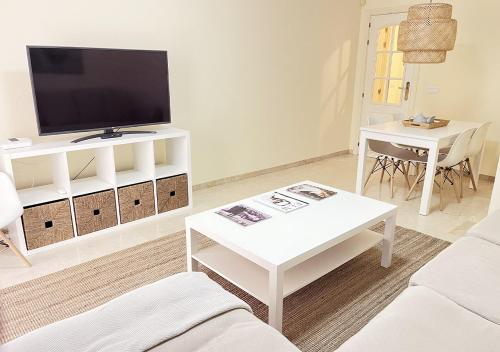 ein weißes Wohnzimmer mit einem TV und einem Tisch in der Unterkunft Apartamento con terraza en primera línea de playa by ISA Hoteles in Estepona