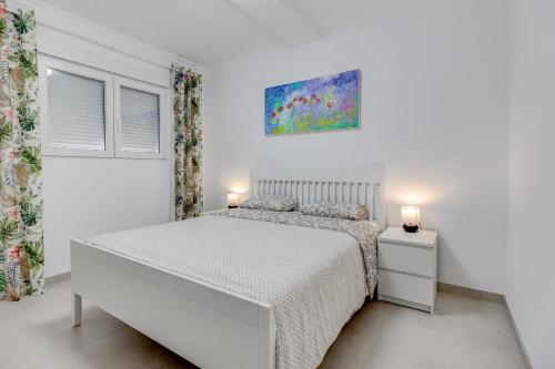 a white bedroom with a white bed and two lamps at Two bedroom apartment near the ocean in Playa de las Americas