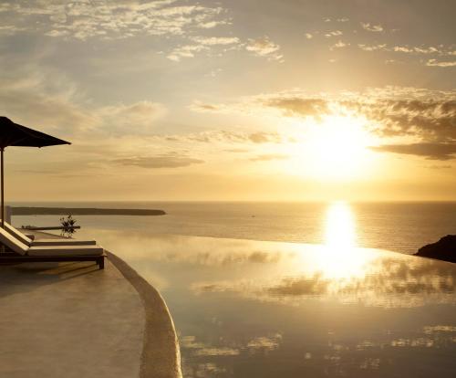 Santo Pure Oia Suites & Villas في أويا: مسبح مع غروب الشمس على المحيط