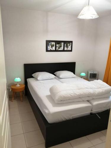 une chambre avec un lit avec des draps blancs et des oreillers dans l'établissement Le soleil d Eugènie appartement dans résidence avec Piscine commune près de Carcassonne, à Olonzac