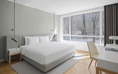 a bedroom with a white bed and a desk and a window at Commune by the Great Wall, in the Unbound Collection by Hyatt in Yanqing