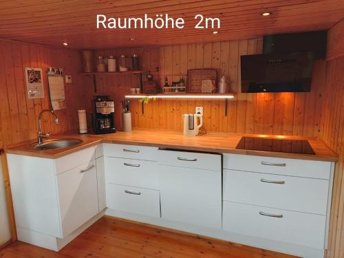 a kitchen with white cabinets and a wooden wall at Harzhexe1 in Güntersberge