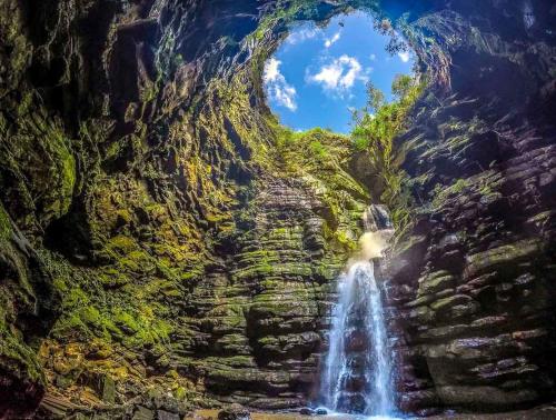 a waterfall in a cave with a large rock wall at Slaviero Ponta Grossa in Ponta Grossa
