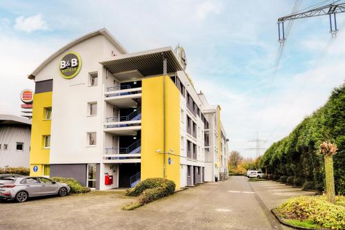 een geel en wit gebouw met een auto buiten geparkeerd bij B&B HOTEL Köln-Frechen in Frechen