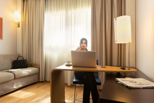a woman sitting at a table with a laptop at Novotel Caserta Sud in Caserta
