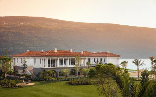 a large white house with a hill in the background at One&Only Portonovi in Herceg-Novi