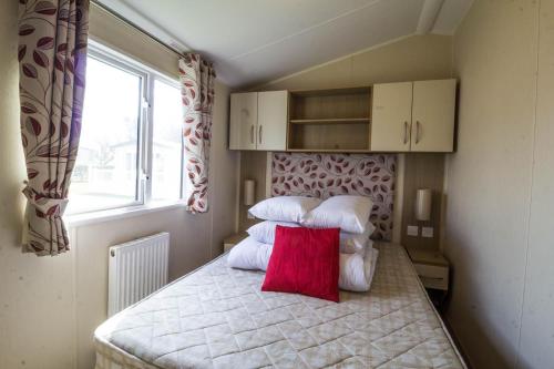 a bedroom with a bed with a red pillow on it at 8 Berth Luxury Caravan With A Full Sea View In Suffolk Ref 20276bs in Hopton on Sea