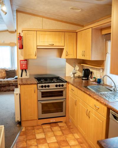 eine Küche mit Holzschränken, einem Herd und einer Spüle in der Unterkunft The Beeches Static Caravan in Cullompton