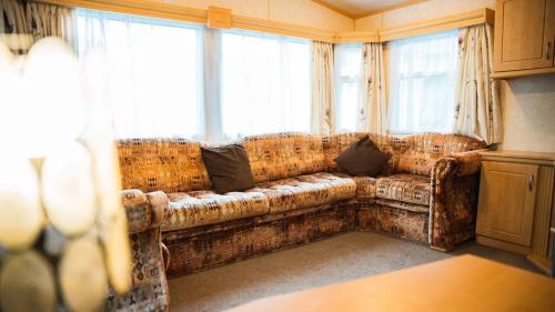 ein Sofa im Wohnzimmer mit Fenstern in der Unterkunft The Beeches Static Caravan in Cullompton
