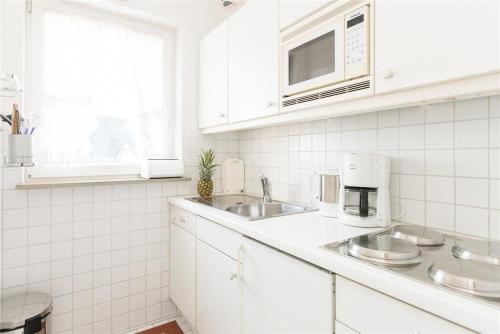 eine weiße Küche mit einer Spüle und einer Mikrowelle in der Unterkunft Haus Ankerlicht 3.OG Wohnung 43 in Westerland