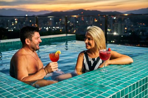 un hombre y una mujer sentados en una piscina con bebidas en Monthez Hotel & Eventos, en Brusque